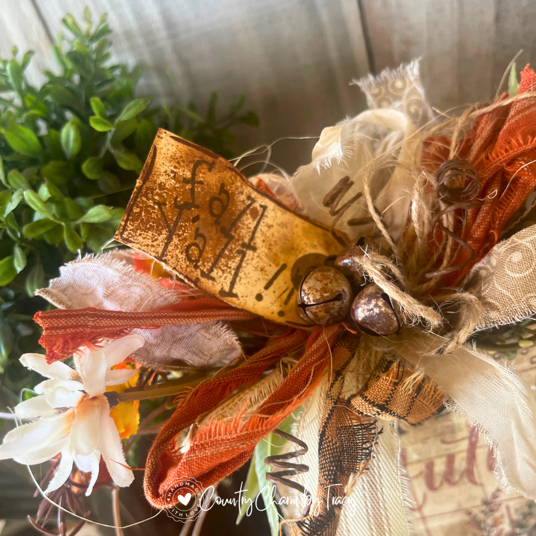 Close up of Hello Autumn Pumpkin Trio Wood Block Decor showing hand-lettered fall yall distressed tag rusty jingle bell cluster curly wire spring and layered brown scroll cream ribbon bow with wispy raffia by Country Charm by Tracy