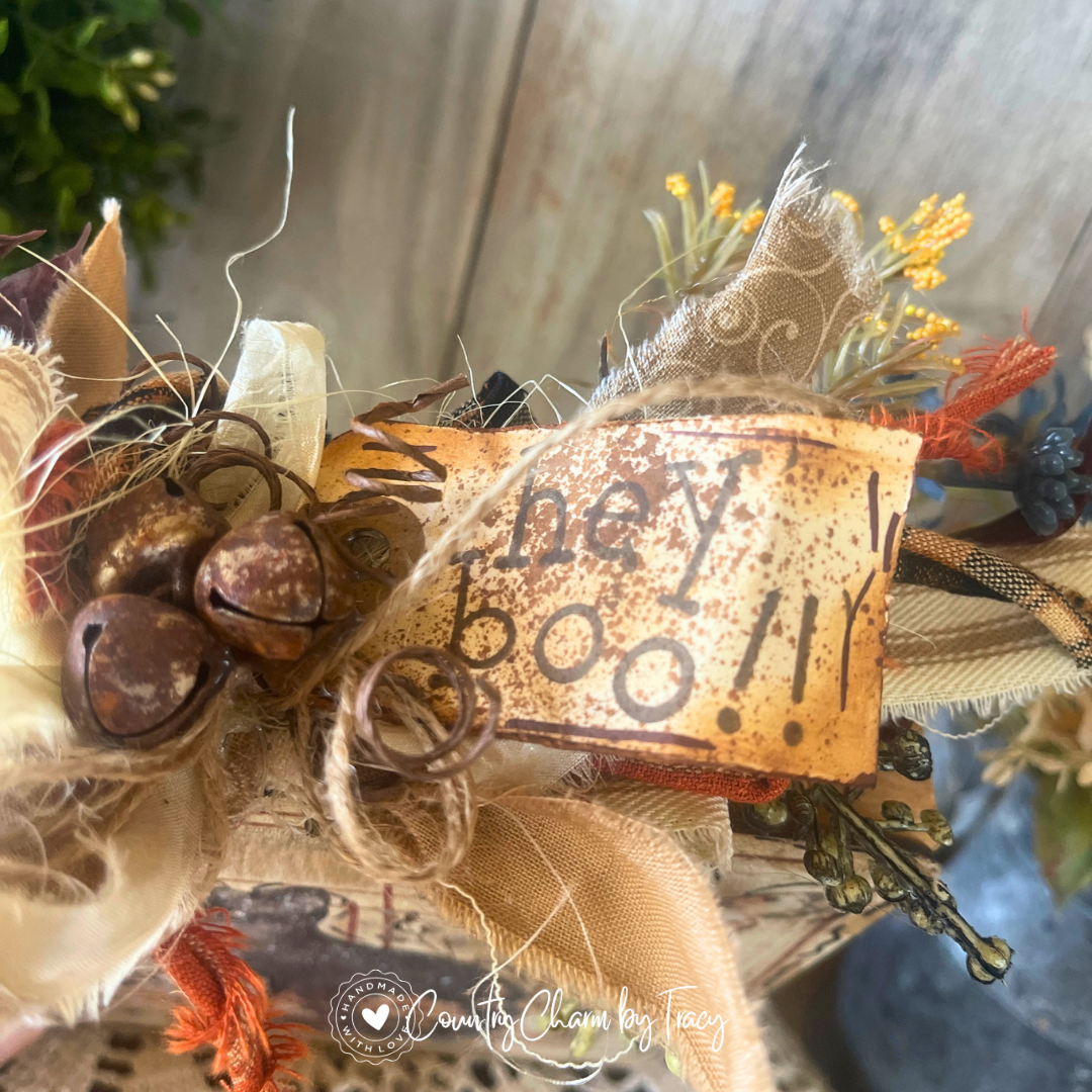 Close up of Hey Boo Black Shorthair Kitty Wood Block Decor showing hand-lettered hey boo distressed tag rusty jingle bell cluster curly wire and layered gold scroll cream ribbon bow with wispy raffia by Country Charm by Tracy