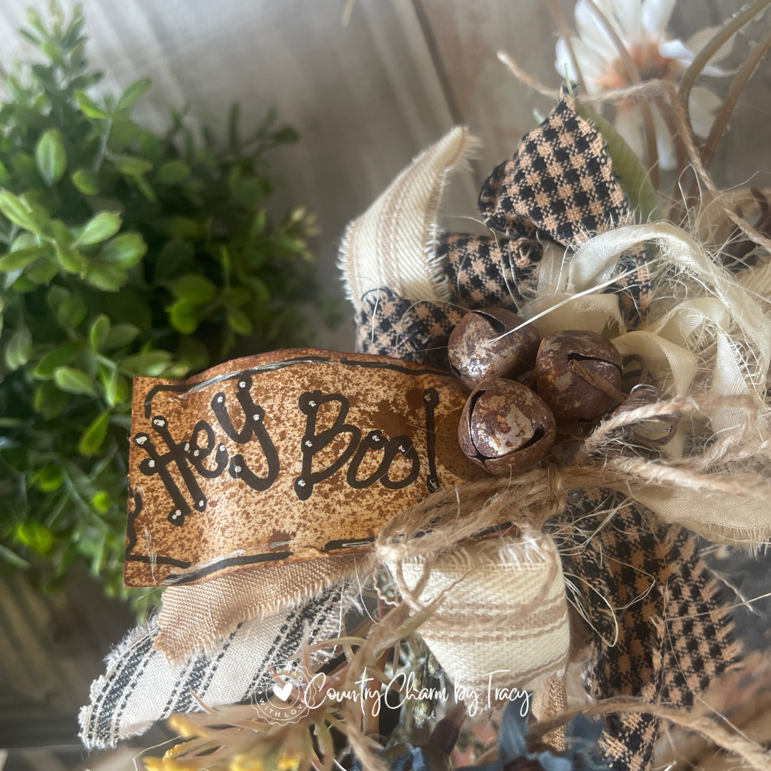 Close up of Hey Boo Black Cat Wood Block Decor showing hand-lettered Hey Boo distressed tag rusty jingle bell cluster layered black plaid and cream newsprint ribbon bow with wispy raffia by Country Charm by Tracy