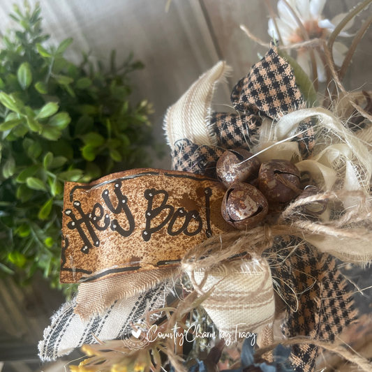 Close up of Hey Boo Black Cat Wood Block Decor showing hand-lettered Hey Boo distressed tag rusty jingle bell cluster layered black plaid and cream newsprint ribbon bow with wispy raffia by Country Charm by Tracy
